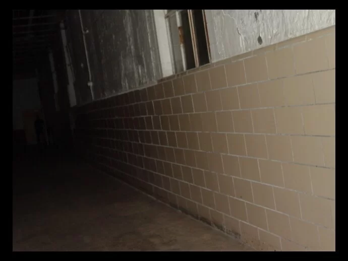 The shadow man peers out of the hallway in front of a yellow door.